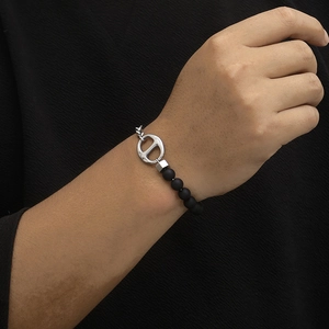 Detailed view of pig nose chain bracelet with CD logo and matte black beads on wrist