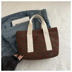 Detail of brown corduroy tote bag with red strawberry patterns and beige handles