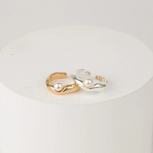 Close-up of gold and silver wavy ear cuffs with pearls on minimalist display