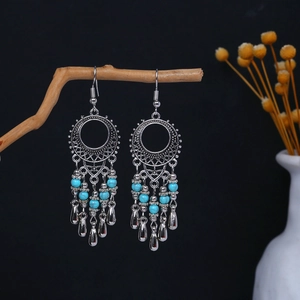 Close-up of vintage silver boho earrings with turquoise beads hanging on a dry branch