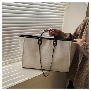 Detail of canvas tote bag with black leather trim and chain strap in natural window light