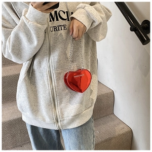 Detail of red heart-shaped patent leather bag with silver chain worn by a model
