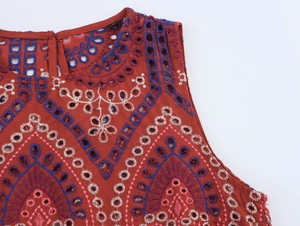 Dettaglio del gilet rosso ruggine con ricamo floreale traforato blu e bianco raffinato