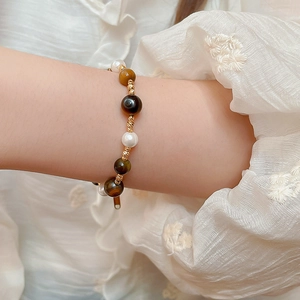 Close-up of pearl and tiger eye beaded bracelet with gold accents on a wrist