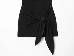 Detail view of black dress featuring a waist tie knot and contrast white stitching