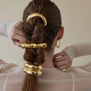 Detail showing golden metal hair ring and textured hair clip on braided brown hair