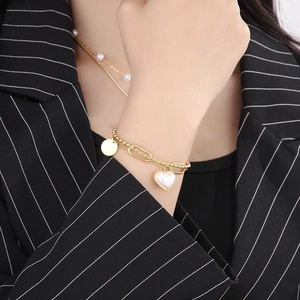 Detail of a gold double-layer bracelet featuring beads, links and heart pearl charm