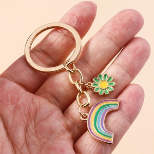 Close-up of golden metal keychain with colorful enamel rainbow and small daisy flower charm