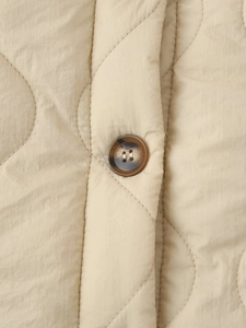 Close-up of beige diamond quilted jacket fabric featuring a brown resin button detail