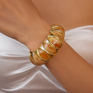Detail of amber resin bangle with gold metal frame worn against champagne silk fabric