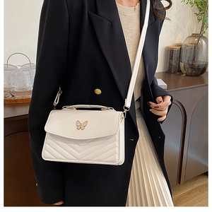 Detail of white quilted crossbody bag featuring a golden butterfly clasp and V-texture
