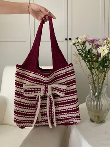 Hand lifting a burgundy and beige striped knitted tote bag with large bow detail