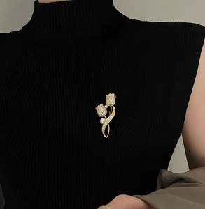 Close-up of a golden tulip brooch with sparkling zircons and pearl on a black sweater