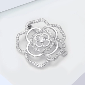 Macro shot of silver hollow camellia brooch with cubic zirconia inlay on white background