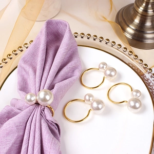 Close-up of golden U-shaped napkin rings featuring elegant double pearls on a silk cloth