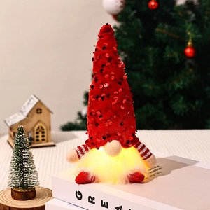 Detail of a red sequined Christmas gnome with warm glowing LED beard on white books