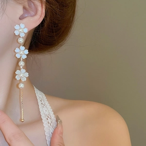 Close-up of elegant long pearl earrings with white floral petals and gold hanging bars