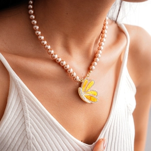 Détail de perles rose champagne et d'un pendentif papillon jaune serti de diamants