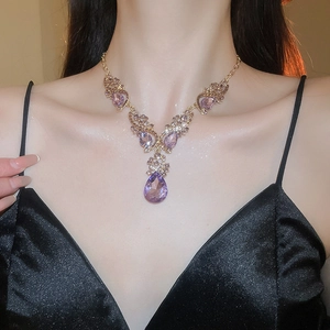 Detail of vintage gold necklace featuring a purple teardrop crystal pendant on neck