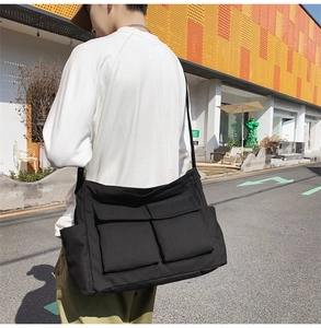 Close-up of black canvas messenger bag with double front pockets on male model