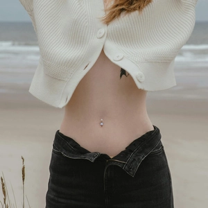 Polished stainless steel belly ring with clear cubic zirconia worn on female model's torso