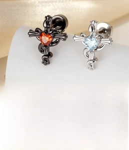 Macro detail of snake wrapped cross earring with red zircon inlay in polished titanium steel