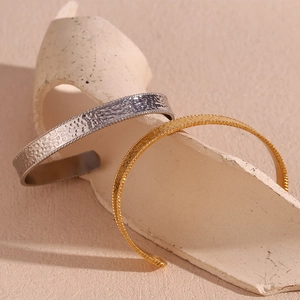 Close-up of hammered gold and silver stainless steel open bangles on minimalist stone