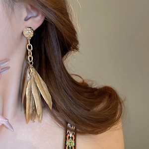 Close-up of vintage gold feather tassel earrings worn by a model in a warm setting