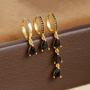 Macro shot of three gold drop earrings with black zircon stones on leather backdrop