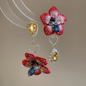Dettaglio di orecchini a fiore ricamati rossi con cristalli blu a goccia e diamanti a cuore