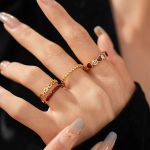 Detail of stacked vintage rings with red enamel hearts and gold chain bands on fingers