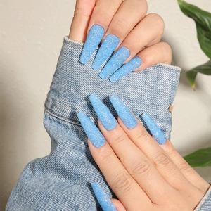 Detail showing long ballerina light blue glitter press-on nails on denim cuff background