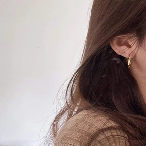 Detail of twisted gold hoop earring on model with elegant minimalist aesthetic