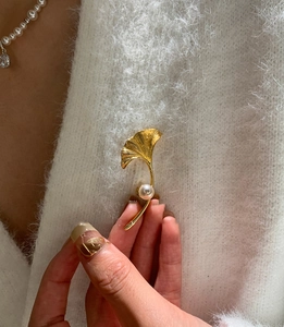Dettaglio della spilla a foglia di ginkgo dorata con perla su maglione mohair