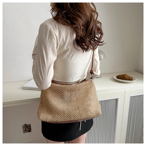 Model wearing a hand-woven straw tote bag with brown base and long leather strap detail