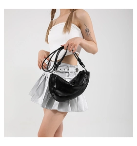 Detail of glossy black crescent shoulder bag featuring stylish knotted strap design