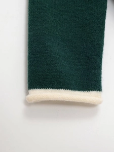 Detailed close-up of dark green knit sweater cuffs with soft cream fleece trim