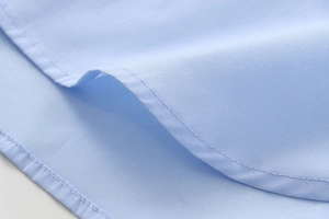 Detailed macro shot of fine stitching on the curved hem of a light blue cotton shirt