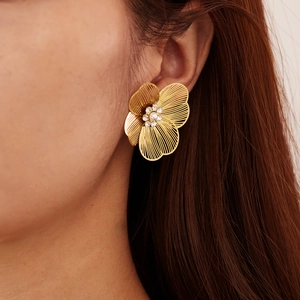 Dettaglio di eleganti orecchini a fiore cavo dorato con perla centrale e strass