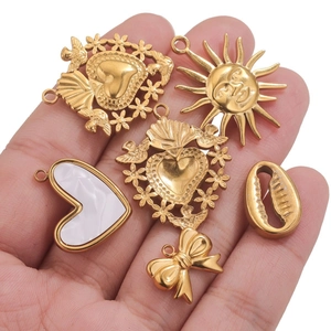 Close-up of assorted gold metal charms including heart and sun designs held in hand
