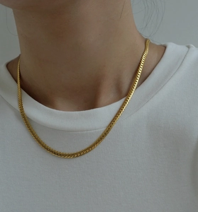 Close-up of golden flat herringbone snake chain necklace on model's neck