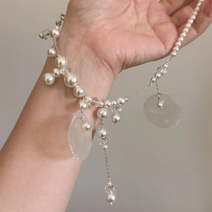 Close-up of pearl and shell pendant necklace with silver chain on female model