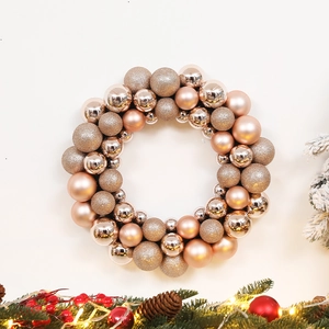 Rose gold Christmas ornament wreath with matte, glossy, and glitter baubles on white background