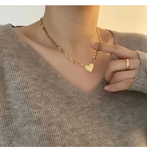 Detail of a gold heart pendant necklace with white enamel inlay worn by a female model