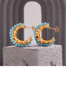 Detailed view of gold-plated C-shaped earrings with turquoise beads on stone base