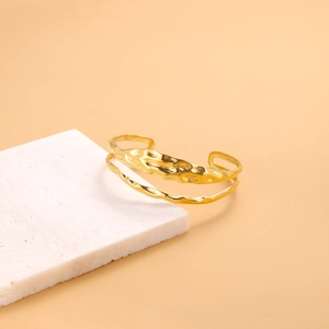 Detailed view of gold-plated open bangle with hammered texture on white stone stand