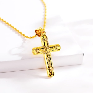 Close-up of golden cross pendant with crucifix detail on a minimal white pedestal