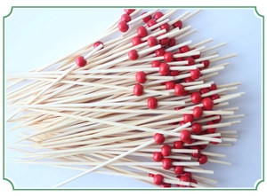 Close-up of bamboo fruit skewers with small red beads on a clean white background