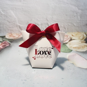 Macro shot of white trapezoidal gift box with deep red ribbon and Love print design