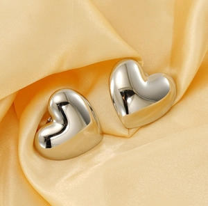 Macro shot of silver heart earrings on golden satin fabric showing polished metal details